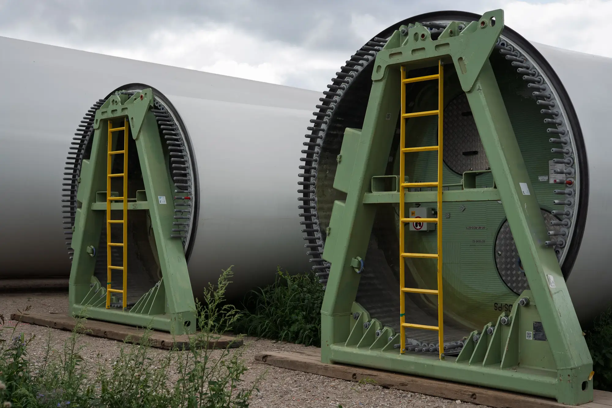 Wind turbine blade roots held in green transport frames on a gravel laydown area